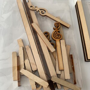 Puede incluir: Un conjunto de piezas de madera para manualidades para construir un modelo. Las piezas son de varias formas y tama&ntilde;os, incluyendo tiras largas, cuadrados cortos y elementos decorativos. Las piezas est&aacute;n hechas de madera de color claro.