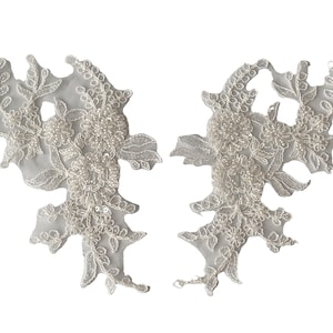 May include: Two white lace appliques with pearl beading and floral designs.