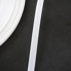 Puede incluir: Borde el&aacute;stico blanco con una superficie texturizada. El borde est&aacute; enrollado en el lado izquierdo de la imagen y colocado plano en el lado derecho de la imagen. El fondo es negro.