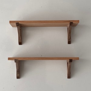 K&ouml;nnte beinhalten: Zwei Holzregale mit einfachen, dunkelbraunen Halterungen. Die Regale sind aus hellem Holz und an einer wei&szlig;en Wand montiert.