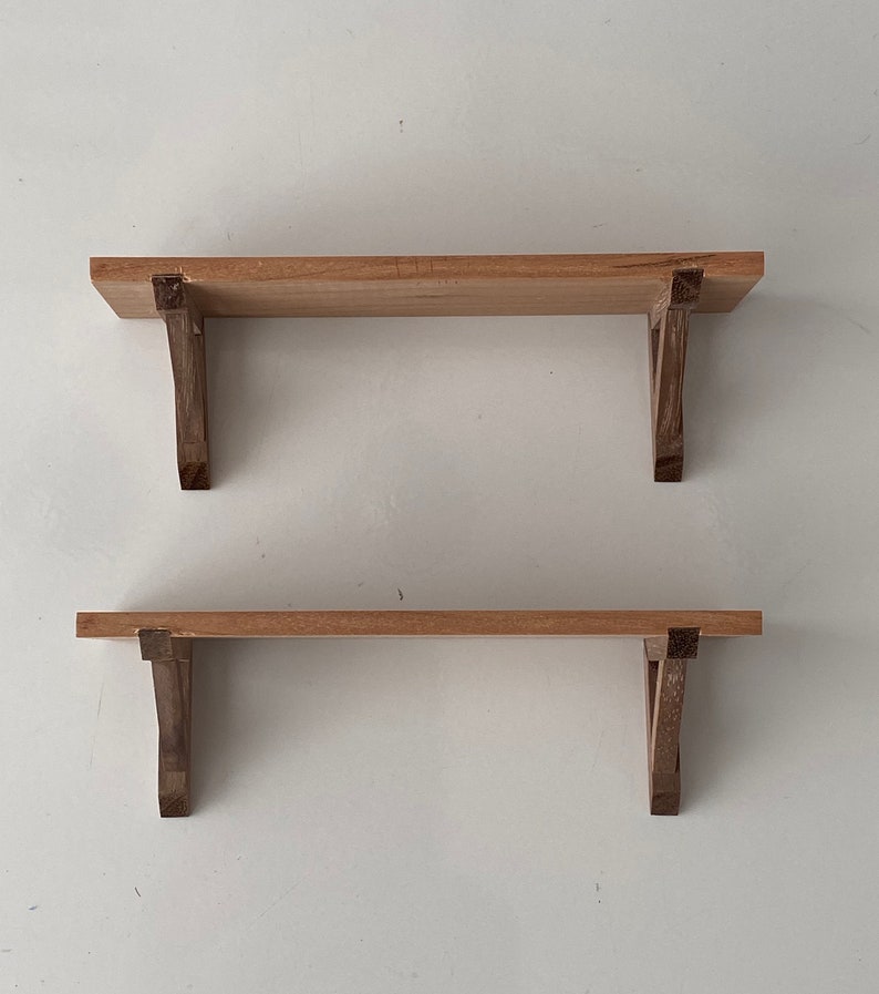 K&ouml;nnte beinhalten: Zwei Holzregale mit einfachen, dunkelbraunen Halterungen. Die Regale sind aus hellem Holz und an einer wei&szlig;en Wand montiert.