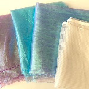 May include: Four pieces of sheer iridescent fabric in shades of purple, blue, and white. The fabric is folded and arranged in a row.