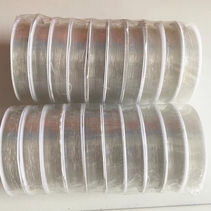 以下が含まれることがあります： 透明な伸縮性のある糸の20個の糸巻きが入ったパッケージ。糸は各糸巻きに巻き付けられ、透明なプラスチックの包装でまとめられています。