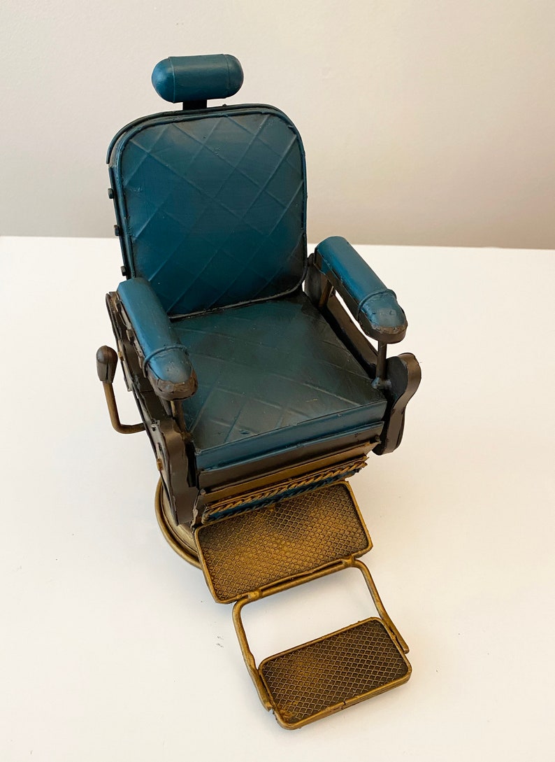 K&ouml;nnte beinhalten: Ein blauer und goldener Metall-Friseurstuhl mit Fu&szlig;st&uuml;tze. Der Stuhl hat einen gepolsterten Sitz und R&uuml;ckenlehne, und die Fu&szlig;st&uuml;tze ist verstellbar.