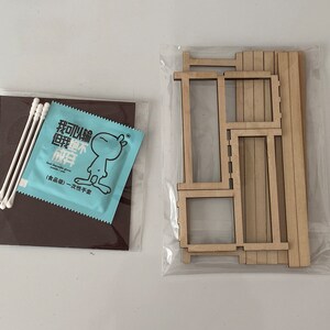Puede incluir: Un conjunto de piezas de madera para construir una casa de mu&ntilde;ecas en miniatura. Las piezas est&aacute;n empaquetadas en una bolsa de pl&aacute;stico transparente. Tambi&eacute;n se incluye un peque&ntilde;o paquete azul de bastoncillos de algod&oacute;n. El paquete tiene texto chino que dice "Puedo construir un hogar feliz".