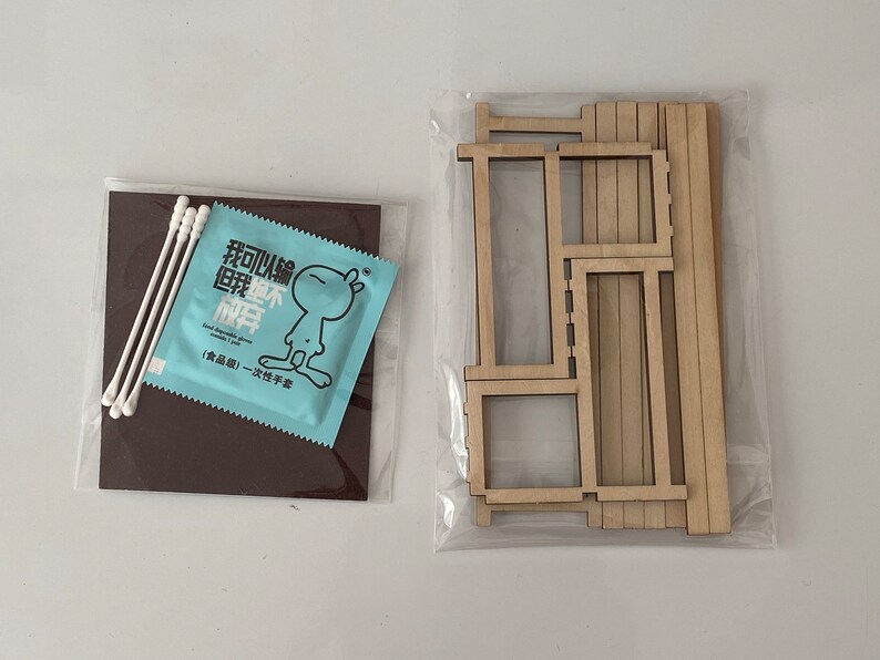 Puede incluir: Un conjunto de piezas de madera para construir una casa de mu&ntilde;ecas en miniatura. Las piezas est&aacute;n empaquetadas en una bolsa de pl&aacute;stico transparente. Tambi&eacute;n se incluye un peque&ntilde;o paquete azul de bastoncillos de algod&oacute;n. El paquete tiene texto chino que dice "Puedo construir un hogar feliz".