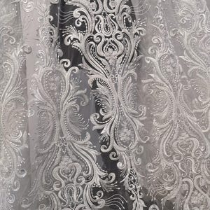 Puede incluir: Tela blanca bordada con un patr&oacute;n floral detallado y ornamentado. El dise&ntilde;o presenta hojas arremolinadas, flores y otros elementos decorativos. La tela parece transparente, con una calidad ligera y aireada, adecuada para cortinas o fines decorativos.
