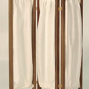 Peut inclure: Un paravent pliable à trois panneaux avec un cadre en bois foncé et des inserts en tissu blanc. L'écran est articulé avec du matériel de couleur laiton. Le tissu est froncé en haut et en bas, créant un effet drapé. Le design est simple et élégant.