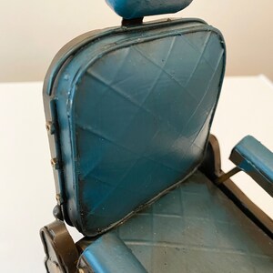K&ouml;nnte beinhalten: Ein blauer Friseurstuhl mit einem Sitz mit Rautenmuster und einer gepolsterten Kopfst&uuml;tze. Der Stuhl ist aus Metall und hat einen Vintage-Look.