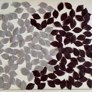May include: A collection of gray and dark brown felt leaves scattered on a white surface. The leaves are arranged in two groups, with the gray leaves on the left and the dark brown leaves on the right.