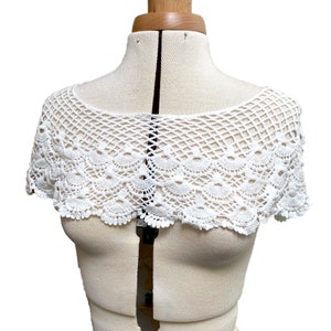 May include: White crocheted lace collar with a scalloped edge. The collar is displayed on a white dress form.