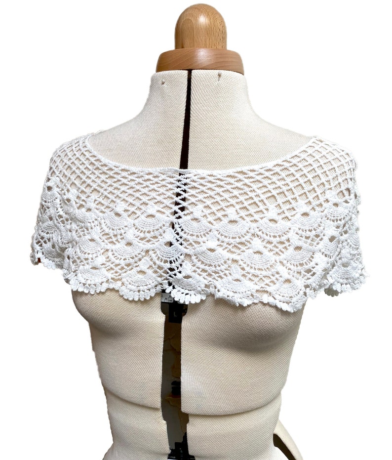 May include: White crocheted lace collar with a scalloped edge. The collar is displayed on a white dress form.