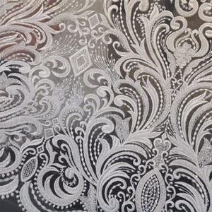 Puede incluir: Primer plano de tela de encaje blanco con un intrincado dise&ntilde;o floral y de volutas. El encaje presenta patrones en relieve y texturizados y acentos brillantes, creando una apariencia delicada y elegante. El dise&ntilde;o incluye formas de diamante y motivos florales detallados.