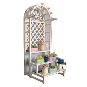 Puede incluir: Un soporte de plantas de madera blanca con un arco de enrejado y tres estantes. Los estantes est&aacute;n decorados con plantas en macetas y flores de varios colores, incluyendo rosa, azul y verde.