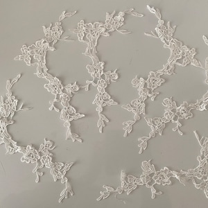May include: White lace appliques featuring floral designs. These delicate lace pieces can be used for embellishing clothing, accessories, or home decor projects.