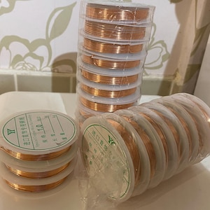 Może przedstawiać: Zbliżenie na dwie szpule drutu miedzianego do tworzenia biżuterii. Szpule są oznaczone po japońsku i angielsku tekstem "Special Copper Wire for Jewelry" i "进口首饰专用铜线".