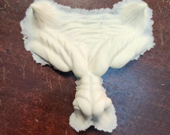 Peut inclure: Une sculpture texturée de couleur crème avec un design abstrait unique. La pièce présente une forme centrale bulbeuse avec des textures organiques détaillées et un bord évasé et froncé. La surface de la sculpture semble douce et souple.