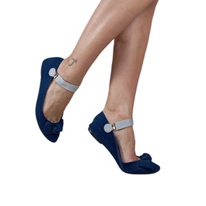 Könnte beinhalten: Ein Paar dunkelblaue Ballerinas mit einem silbernen Glitzer-Knöchelriemen und einer Schleife an der Spitze.