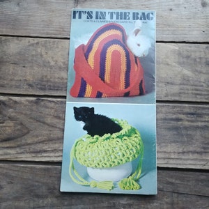 Peut inclure: Un livret de modèles de crochet intitulé "It's in the Bag" de Coats & Clark's Studio Card No. 7. Le livret présente deux images de sacs au crochet avec des chatons à l'intérieur. Le premier sac est arc-en-ciel et le second sac est vert.