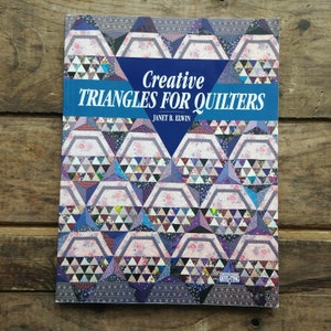 May include: Book cover with a blue and white title "Creative Triangles for Quilters" by Janet B. Elwin. The cover features a colorful quilt pattern with a variety of triangles in shades of purple, pink, blue, and green.