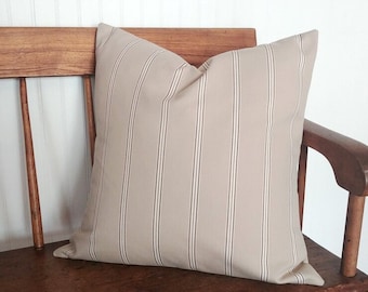 May include: A beige and brown striped throw pillow on a wooden bench. The pillow is made of a soft, woven fabric with a subtle sheen.
