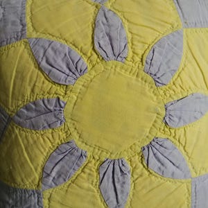 May include: A close-up of a yellow and purple quilt with a sunburst pattern. The quilt is made of fabric squares sewn together to create a design.