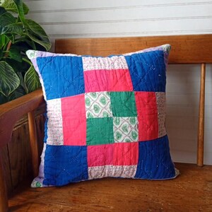 May include: A square patchwork cushion featuring a grid of fabric squares in solid blue, bright red, and vibrant green, interspersed with squares of a light-coloured floral print. The entire surface is finished with a diamond-shaped quilted stitch pattern.