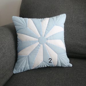 May include: A light blue and white quilted cushion with a starburst design. The cushion has the number "2" printed on it.