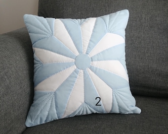 May include: A light blue and white quilted pillow with a starburst design. The pillow has a number "2" printed on it.