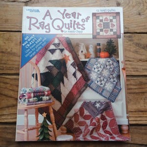 May include: A book cover titled "A Year of Rag Quilts" by Annis Clapp. The cover features images of various rag quilts in different patterns and colors, including red, white, and blue. The book also includes instructions for making pillows and larger quilts.