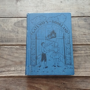 May include: A blue book with the title "GATEWAYS TO BOOKLAND" on the cover. The cover features an illustration of a gate opening to reveal a castle in the distance. Two children, a boy and a girl, are standing in front of the gate.