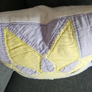 May include: A purple and yellow patchwork pillow with a starburst design. The pillow is made of quilted fabric and has a white backing.