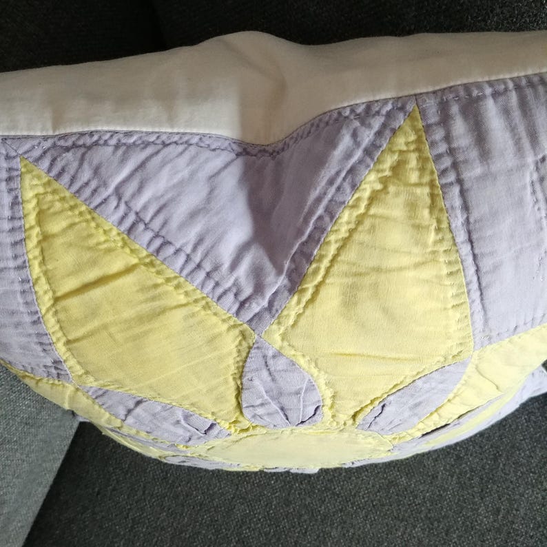 May include: A purple and yellow patchwork pillow with a starburst design. The pillow is made of quilted fabric and has a white backing.