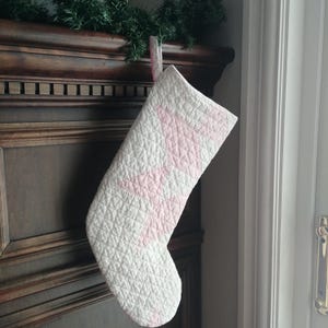Peut inclure: Une chaussette de Noël blanche matelassée avec des étoiles en patchwork rose accrochée à une cheminée en bois.
