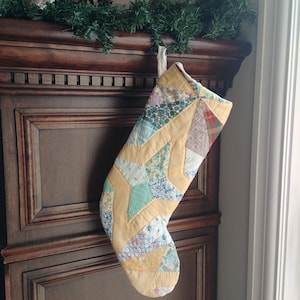 Könnte beinhalten: Ein Patchwork-Weihnachtsstrumpf mit einem Sternmuster in Gelb, Blau und Grün. Der Strumpf hängt an einem Holzmantel.