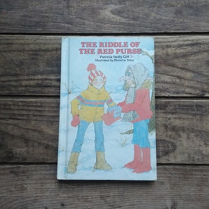 May include: A vintage children's book titled "The Riddle of the Red Purse" by Patricia Reilly Giff, illustrated by Blanche Sims. The cover features a girl and a woman in winter clothing.