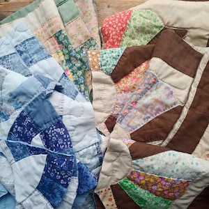 May include: A patchwork quilt featuring a fan-shaped pattern with various fabric segments. The left side displays shades of blue, white, and light green floral prints, while the right side incorporates brown, cream, and multi-coloured floral patterns.