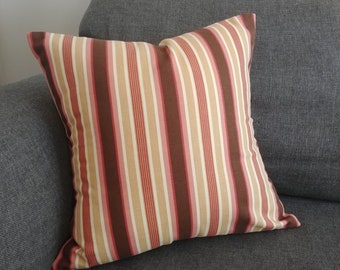 May include: A striped cushion with brown, pink and cream stripes. The cushion is on a grey sofa.