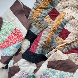 May include: A patchwork quilt featuring a variety of fabric patterns including floral, paisley, and geometric prints in shades of brown, red, yellow, blue, and green. The textile displays intricate stitching and multiple fabric squares joined together.