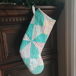 May include: A teal and white patchwork Christmas stocking with a pink and white floral pattern.