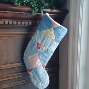 Peut inclure: Une chaussette de Noël en patchwork bleu, rose et jaune avec des fleurs brodées rouges.