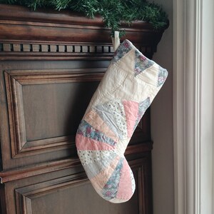 May include: A white and pink patchwork Christmas stocking with floral patterns. The stocking is hanging on a dark wood surface.