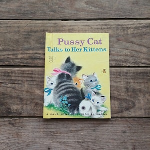 May include: A vintage children's book titled "Pussy Cat Talks to Her Kittens" with a yellow cover and an illustration of a mother cat and her kittens. The book is part of the Rand McNally Junior Elf Book series.