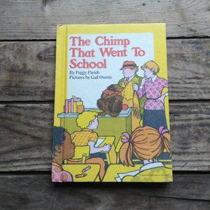 May include: A yellow book cover with the title "The Chimp That Went To School" by Peggy Parish. The cover features illustrations of a chimpanzee, a teacher, and children in a classroom.