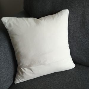May include: A white pillow with a plain design. The pillow is sitting on a dark gray couch.