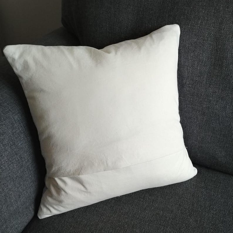May include: A white pillow with a plain design. The pillow is sitting on a dark gray couch.