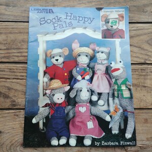 May include: A book titled "Sock Happy Pals" featuring 6 nostalgic patterns by Barbara Finwall. The cover shows a group of sock puppets, including a pig, a bunny, a cat, a frog, a sheep, and a dog. Each puppet is dressed in different clothes and accessories.