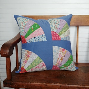 May include: A blue patchwork cushion with a floral design. The cushion is made of different fabrics and has a quilted look. It is sitting on a wooden bench.