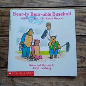 May include: A children's book titled "Bear-ly Bear-able Baseball" with illustrations of bears playing baseball. The cover features the text "Riddles, Jokes, and Knock-Knocks" and the author's name, Mort Gerberg. The Scholastic logo is at the bottom.