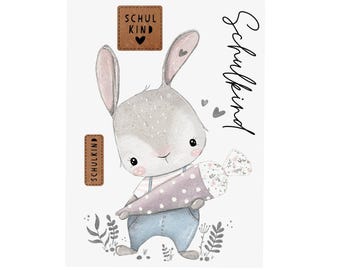 Könnte beinhalten: Aquarell-Illustration eines grauen Hasen mit blauer Latzhose, der eine lila-weiße, kegelförmige Süßigkeitentüte hält. Das Bild enthält den Text "Schulkind" und zwei braune Etiketten mit dem Text "Schul Kind".